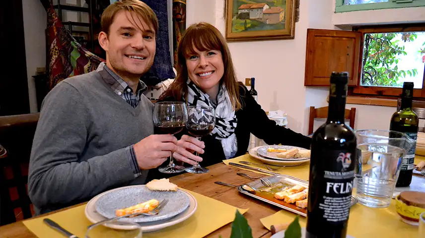 Couple of young people toasting with chianti in front of a table set for a typical Tuscan lunch